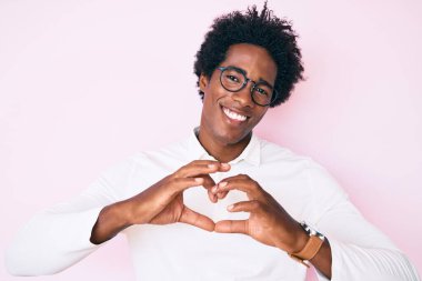 Afro saçlı, iş gömleği ve gözlüklü, aşık bir şekilde gülümseyen ve elleriyle kalp sembolü yapan yakışıklı Afro-Amerikan erkeği. romantik kavram. 