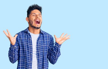 Yakışıklı Latin Amerikalı genç adam gündelik tişört giyiyor deli gibi bağırıyor ve bağırıyor agresif bir ifade ve kollar havada. hüsran kavramı. 