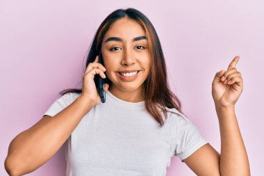 Genç Latin kadın akıllı telefonda konuşuyor gülümsüyor mutlu bir şekilde el ve parmak kenarı işaret ediyor. 