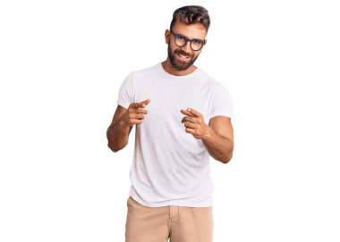 Gündelik kıyafetler giyen ve gözlüklü genç İspanyol adam mutlu ve komik yüzlü parmaklarını kameraya doğrultuyor. iyi enerji ve titreşimler. 