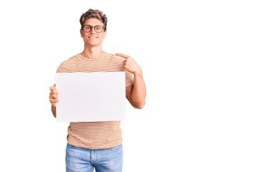 Boş pankart tutan yakışıklı genç adam mutlu ve gururlu bir kendini işaret ediyor. 