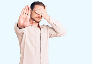 Genç, beyaz, sıradan kıyafetler giyen, elleriyle gözleri kapatan, üzgün ve korku dolu hareketler yapan yakışıklı bir adam. utangaç ve olumsuz kavram. 