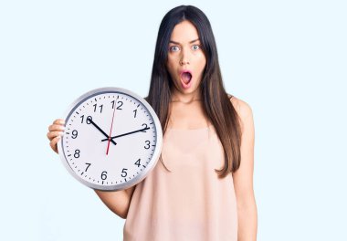 Genç, güzel, beyaz bir kadın, elinde büyük bir saat tutuyor. Şaşırmak için ağzı açık, korkmuş ve şaşırmış. İnanmayan yüz. 