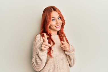 Kış süveteri giyen genç, güzel, kızıl saçlı bir kadın mutlu ve komik yüzüyle kamerayı işaret ediyor. iyi enerji ve titreşimler. 