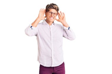 İş kıyafetleri ve gözlük takan genç yakışıklı adam iki elini de kulak hareketlerinde duymaya çalışıyor, dedikoduya meraklı. İşitme sorunu, sağır 