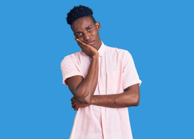 Genç, Afro-Amerikalı bir adam günlük kıyafetler giyip kollarını kavuşturup depresyondan sıkılmış ve yorgun görünüyor.. 
