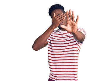 Genç, Afro-Amerikan bir adam, günlük kıyafetler giyiyor, elleriyle gözleri örtüyor ve üzgün ve korku ifadeleriyle jestleri durduruyor. utangaç ve olumsuz kavram. 