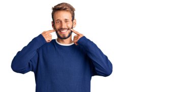 Sakallı, sıradan süveter giyen, ağzı açık gülümseyen, parmakları işaret eden ve neşeli gülümsemeye zorlayan yakışıklı sarışın adam. 