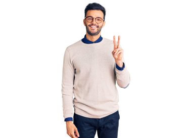 Zarif kıyafetler ve gözlük takan yakışıklı İspanyol adam iki numarayı gösterip işaret ederken kendine güvenen ve mutlu bir şekilde gülümsüyor.. 