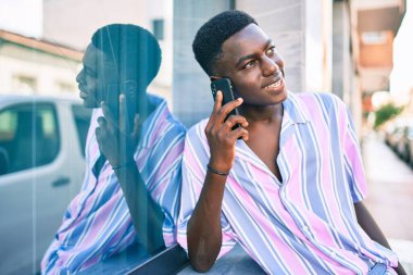 Genç Afrikalı Amerikalı gülümseyen adam şehrin caddesindeki akıllı telefonda mutlu bir şekilde konuşuyor..