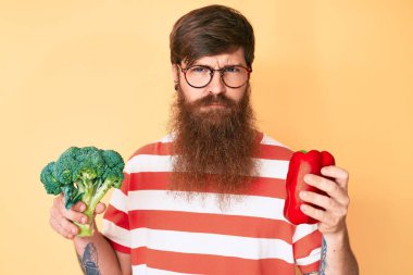 Uzun sakallı, elinde brokoli ve kırmızı biber olan yakışıklı genç bir adam. Depresyonda ve endişeli, sinirli ve korkmuş. hüzünlü ifade. 