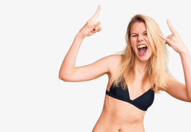 Bikini giyen, çılgın bir ifadeyle bağıran genç, güzel sarışın kadın elleri havada rock sembolü yapıyor. Müzik yıldızı. ağır müzik konsepti. 