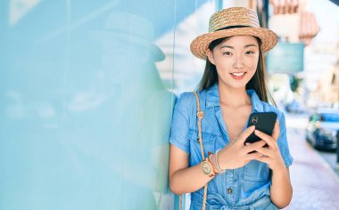 Genç Çinli turist şehrin duvarına dayanmış akıllı telefon kullanıyor..