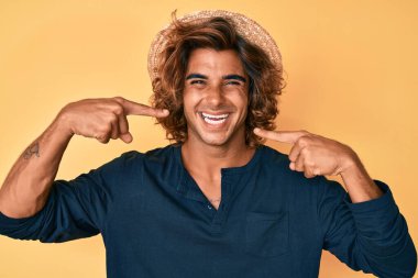 Yazlık şapkalı, neşeli gülümseyen, parmaklarıyla ve ağzıyla işaret eden İspanyol bir genç. diş sağlığı kavramı. 