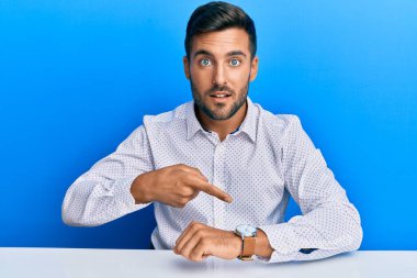 Masada oturan yakışıklı İspanyol iş elbiseli adam saati izlemek için acele ediyor, sabırsız, geç kaldığı için kızgın ve sinirli. 