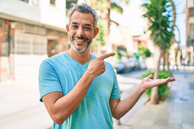 Şehrin caddesinde günlük giysiler giyen orta yaşlı, gri saçlı bir adam kameraya hayret ediyor ve gülümsüyor.. 