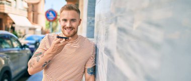 Genç İrlandalı gülümseyen mutlu bir adam şehrin caddesinde akıllı telefonda konuşuyor..