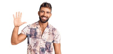 İspanyol asıllı genç adam yaz kıyafetleri giyip beş numarayı gösterip işaret ederken kendinden emin ve mutlu gülümsüyor.. 