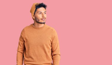 Kış süveteri ve yün şapka giyen yakışıklı Latin Amerikalı genç adam yüzünde tebessümle yan yana bakıyor, doğal bir ifade. Kendinden emin gülen. 