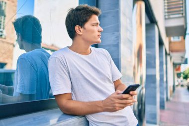 Beyaz adam şehirde akıllı telefon kullanarak mutlu bir şekilde gülümsüyor..