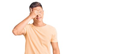 Genç ve yakışıklı bir adam, sıradan kıyafetler giyip gözlerini eliyle kapatıyor, ciddi ve üzgün görünüyor. Görme, saklama ve reddetme konsepti 