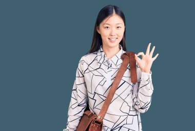 Genç, güzel Çinli bir kadın evrak çantası tutuyor. Parmaklarıyla imza atıyor, gülümsüyor. Mükemmel bir sembol. 