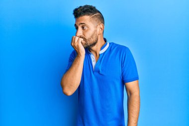 Sakallı, sıradan kıyafetler giyen, gergin ve ağzı tırnak yiyen yakışıklı bir adam. anksiyete. 