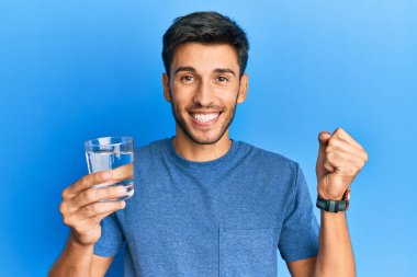 Genç yakışıklı adam bir bardak su içiyor gururla bağırıyor, zaferi kutluyor ve başarıyı kollarını kaldırarak kutluyor. 