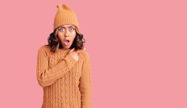 Yün kazak ve kış şapkası giyen genç, güzel, melez bir kadın parmaklarını yana uzatarak şaşırdı, ağzı açık şaşkın bir ifade takındı.. 