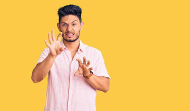 Yakışıklı Latin Amerikalı genç adam rahat bir yaz gömleği giyiyor komik bir şekilde gülüyor kedi gibi pençe hareketi yapıyor, agresif ve seksi bir ifade. 