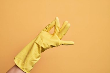 İzole edilmiş sarı arka plan üzerinde temizlik eldivenli beyaz bir gencin eli başarı için parmaklarını şıklatıyor, kolay ve eliyle sembol jestine tıklıyor.