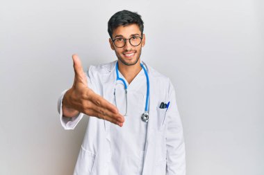 Doktor üniforması giyen ve steteskop takan genç yakışıklı adam selamlama ve hoş geldin demek için dostça tokalaşıyor. başarılı iş. 