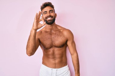 Genç İspanyol üstsüz gülümseyen adam el ve parmaklarıyla imza atıyor. başarılı ifade. 