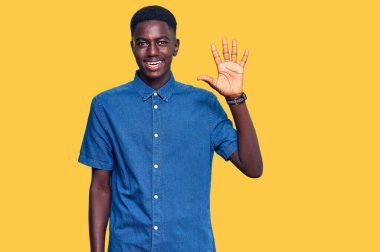 Genç Afro-Amerikalı günlük kıyafetler giymiş beş numarayı gösterip işaret ederken kendinden emin ve mutlu bir şekilde gülümsüyor.. 