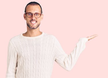 Genç, yakışıklı, günlük kıyafetler ve gözlük takan neşeli bir şekilde gülümseyen ve avuç içi kameraya bakan bir adam.. 