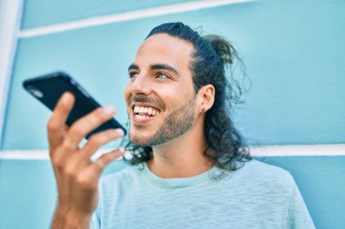 Genç İspanyol adam gülümsüyor. Akıllı telefonda konuşuyor. Duvara yaslanıyor.