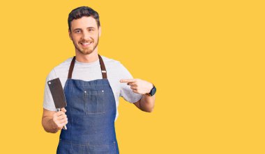 Profesyonel önlük giymiş yakışıklı genç adam elinde bıçakla gülümseyen mutlu ve gururlu birini işaret ediyor. 