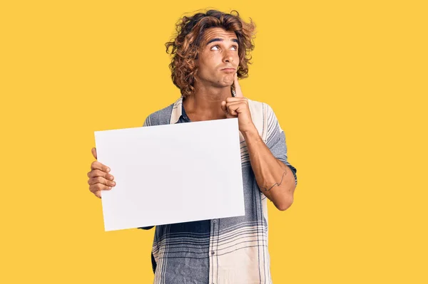 Jovem Hispânico Segurando Banner Vazio Branco Rosto Sério Pensando Questão — Fotografia de Stock