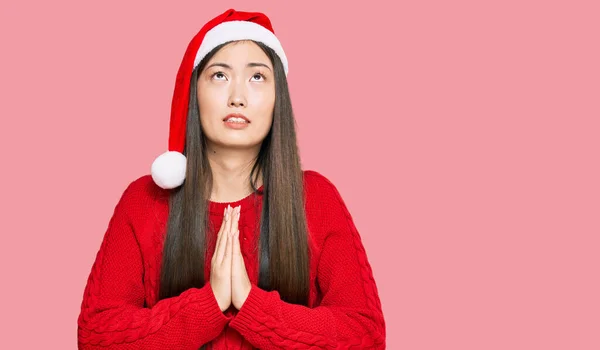クリスマスの帽子をかぶっている若い中国の女性は 手で物乞いと祈りをし 顔に希望の表情とともに非常に感情的で心配しています お願い — ストック写真
