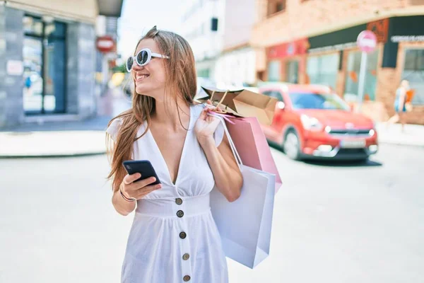 Mladá Blondýna Žena Úsměvem Šťastný Držení Nákupních Tašek Pomocí Smartphone — Stock fotografie