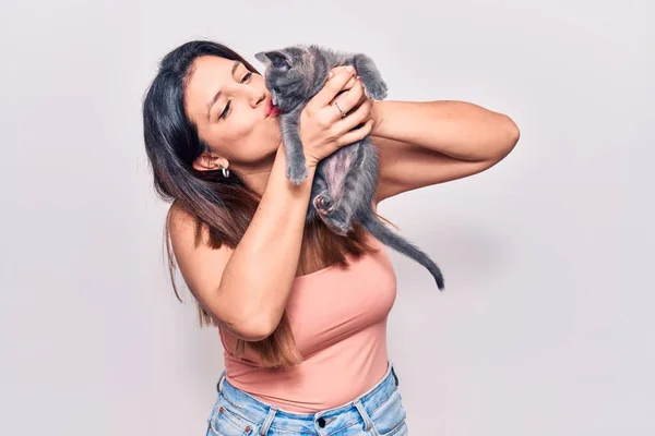 Young beautiful latin woman smilling happy. Standing with smile on face holding and kissing adorable cat over isolated white background