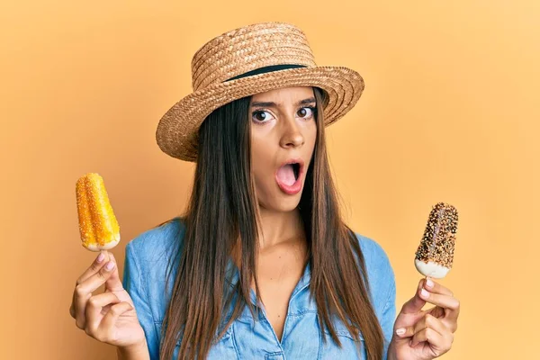 衝撃の顔でアイスクリームを保持夏のスタイルを身に着けている若いヒスパニック系の女性 懐疑的で皮肉を探して オープン口で驚いて — ストック写真