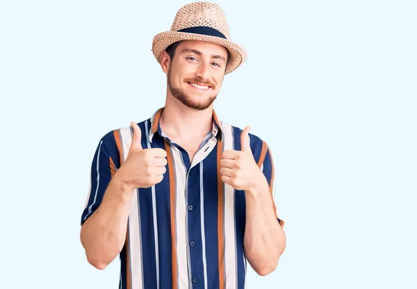 夏の帽子の成功の印を身に着けている若いハンサムな白人男性は手で肯定的なジェスチャーをし 親指を上げて笑顔と幸せ 陽気な表情と勝者のジェスチャー — ストック写真