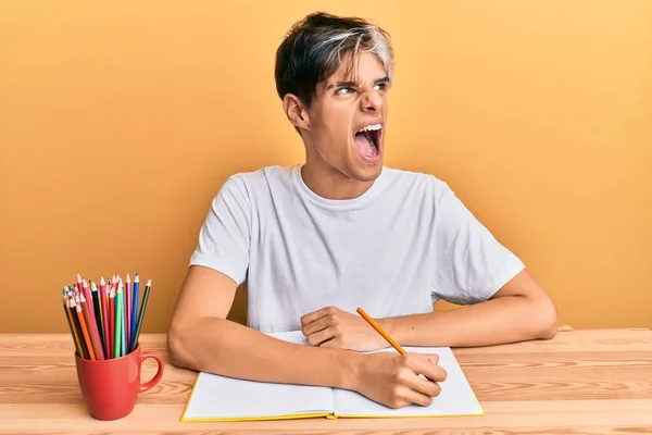 Jovem Hispânico Escrevendo Livro Sentado Mesa Irritado Louco Gritando Frustrado — Fotografia de Stock