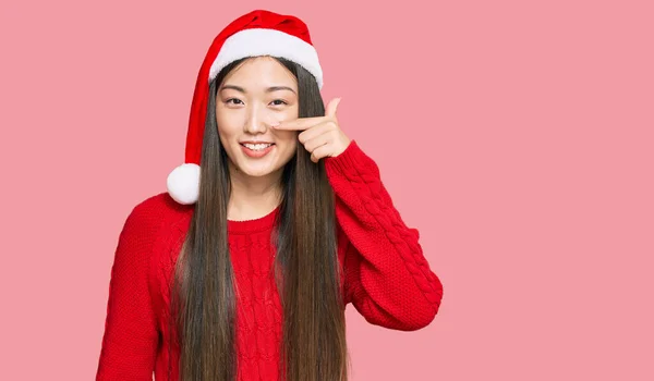 若い中国の女性が顔や鼻に手指で指してクリスマスの帽子をかぶって 陽気に笑っている 美の概念 — ストック写真