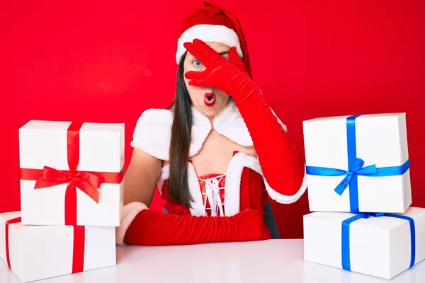 Молодая Женщина Костюме Санта Клауса Сидит Столом Подарками Подглядывая Шокирующее — стоковое фото