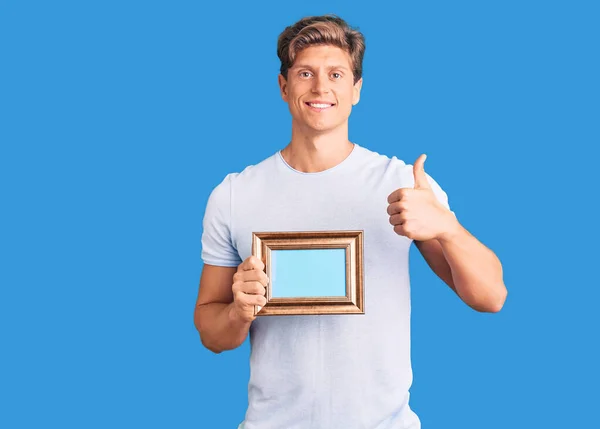 Joven Hombre Guapo Sosteniendo Marco Vacío Sonriendo Feliz Positivo Pulgar —  Fotos de Stock