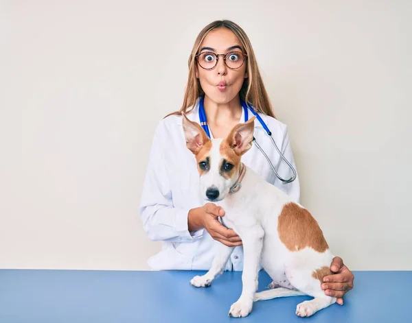 若いです美しいですブロンド獣医師女性チェック犬の健康作り魚顔とともに口と目を細めて クレイジーとコミカル — ストック写真