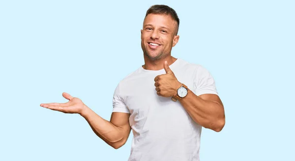 掌の手を示すカジュアルな白いTシャツを着たハンサムな筋肉の男と親指で をジェスチャーを行います 笑顔幸せと陽気な — ストック写真