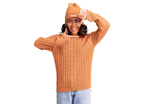 ウールのセーターと冬の帽子を身に着けている若い美しい混合レースの女性は幸せな顔で手や指でフレームを作る笑顔 創造性と写真の概念 — ストック写真